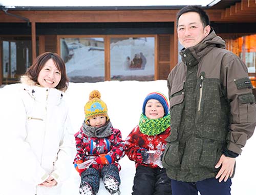 雪景色の中で30代くらいの夫婦とスノーウェアを着た二人の子ども4人でほほ笑む家族写真