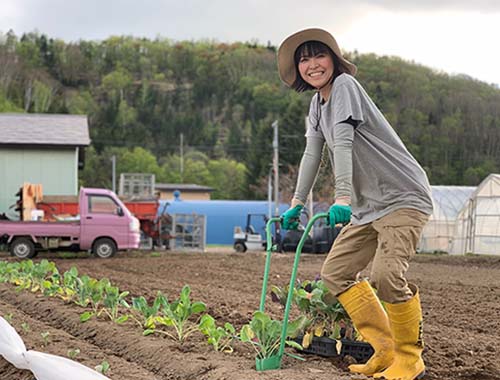 麦わら帽子を被った若い女性が笑顔で畑仕事をしている写真