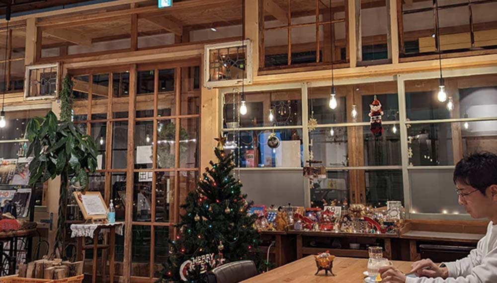 クリスマスの装飾をした木目調の喫茶店の店内と眼鏡をかけた男性