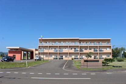 左端には屋根付き乗降車口がある薄いオレンジ色の外壁のケアハウスつべつの外観写真