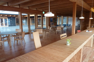 左側には丸いテーブルが並、右側には長いテーブルとそれぞれに椅子があり部屋の外が見えるカフェコーナーの写真