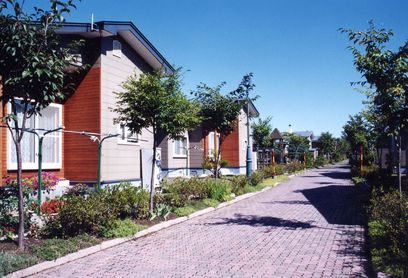 レンガ敷歩道と歩道に沿って整備された植え込みの向こうに並んで建つ平屋建て町営住宅の写真