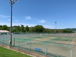 森を背景に青い空の下にある2面のテニスコートの写真
