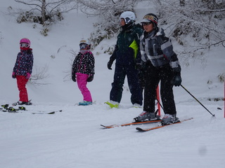 真っ白に雪が降り積もったスキー場で、生徒の皆さんがスキー板を履いて、講師の先生から指導を受けている講習会の様子の写真