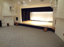 ステージが照明で照らされている中央公民館講堂の写真