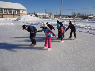 帽子と手袋を付け、防寒着を着た生徒達が氷の上を滑っているスケート教室の様子の写真