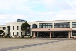 クリーム色の外壁の2階建ての建物で、左側の一部が半円形の造りになっており、中央の玄関前は屋根付きのテラスと数段の階段が設けられている津別小学校の外観写真
