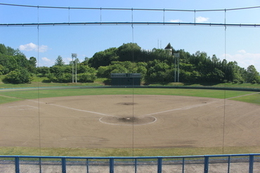 客席から手前にバッターボックスがあり奥に外野が見える運動広場野球場の風景写真